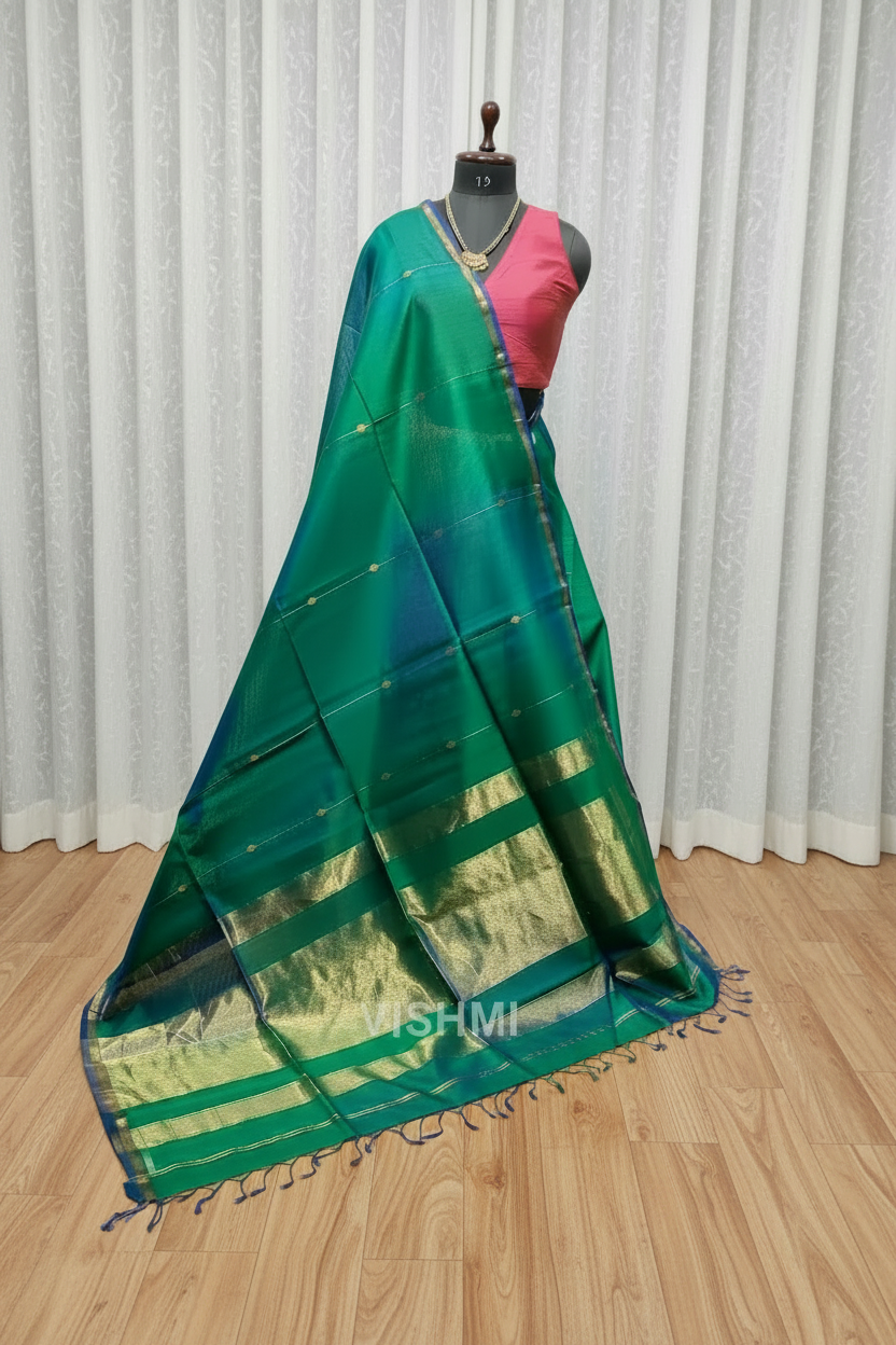 Green saree with gold border on a wooden floor with mannequin and other sarees in the background.