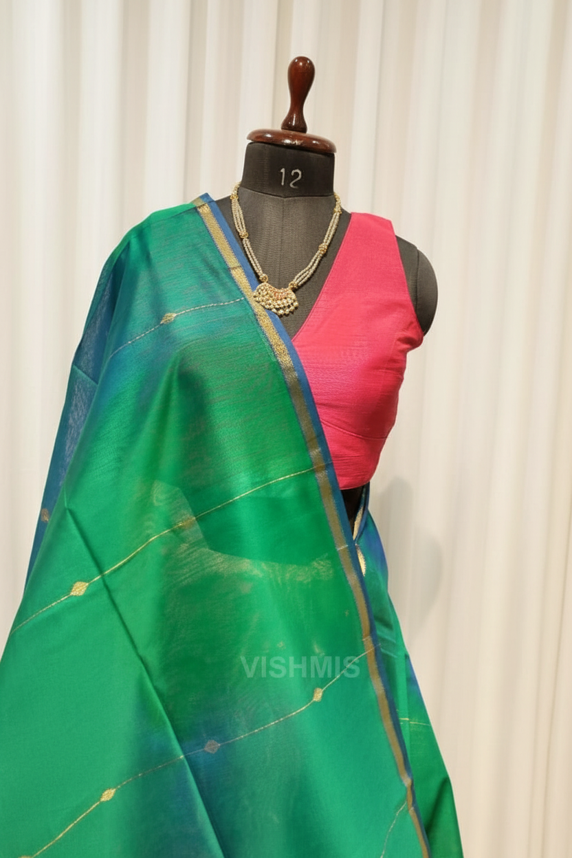 Green saree with pink blouse on a mannequin against a background of colorful sarees.