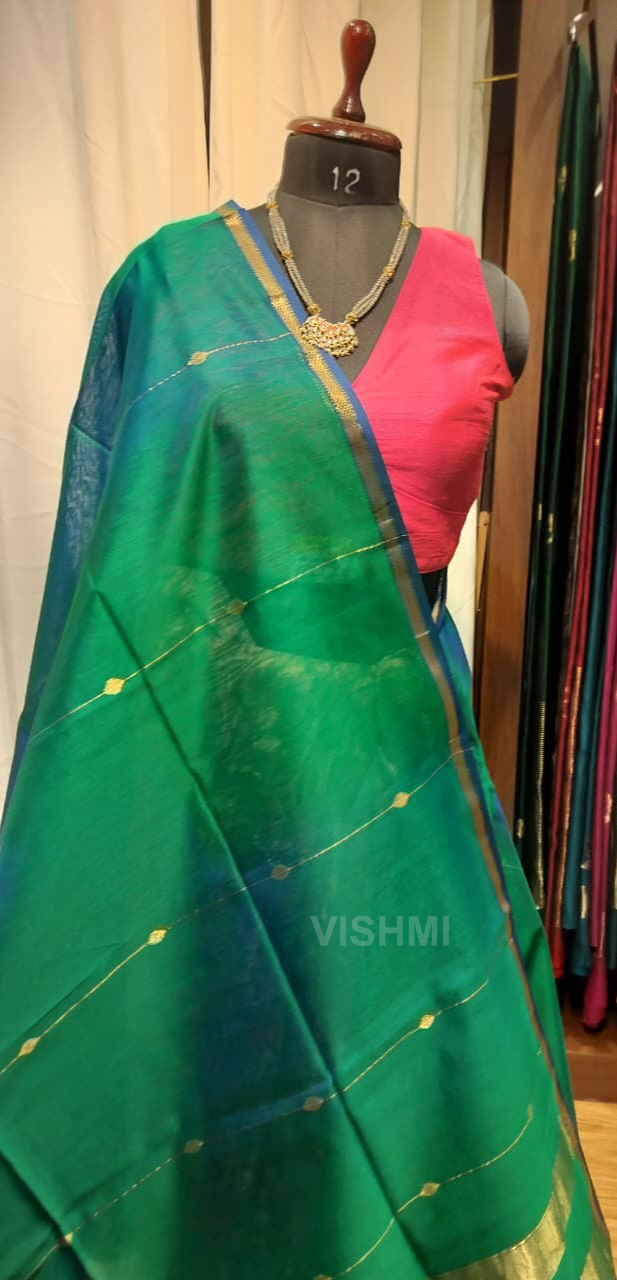 Green saree with gold border on a mannequin, with other sarees in the background.