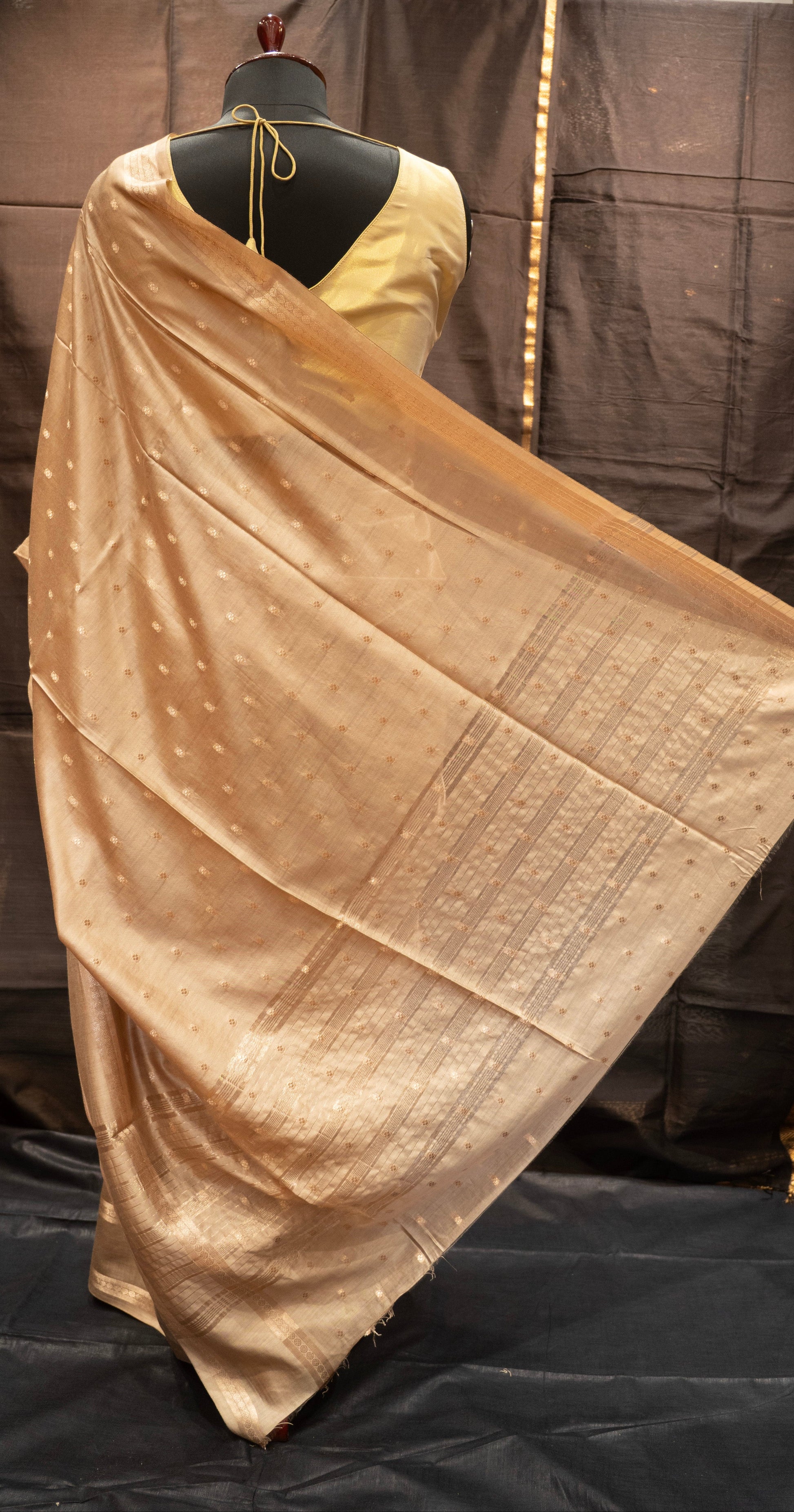 Beige saree draped over a mannequin against a dark background