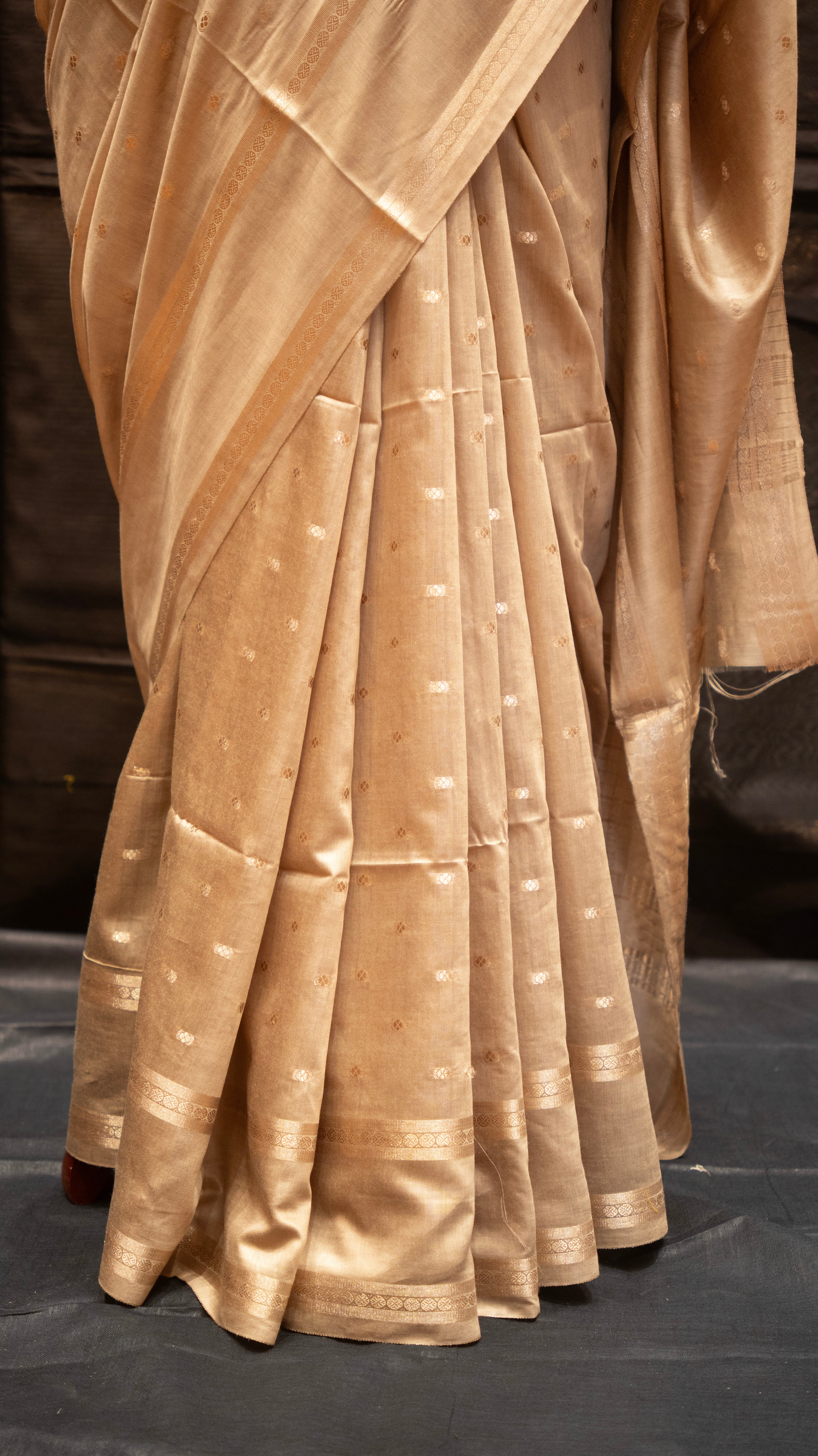 Close-up of a beige saree with a subtle pattern on a dark background