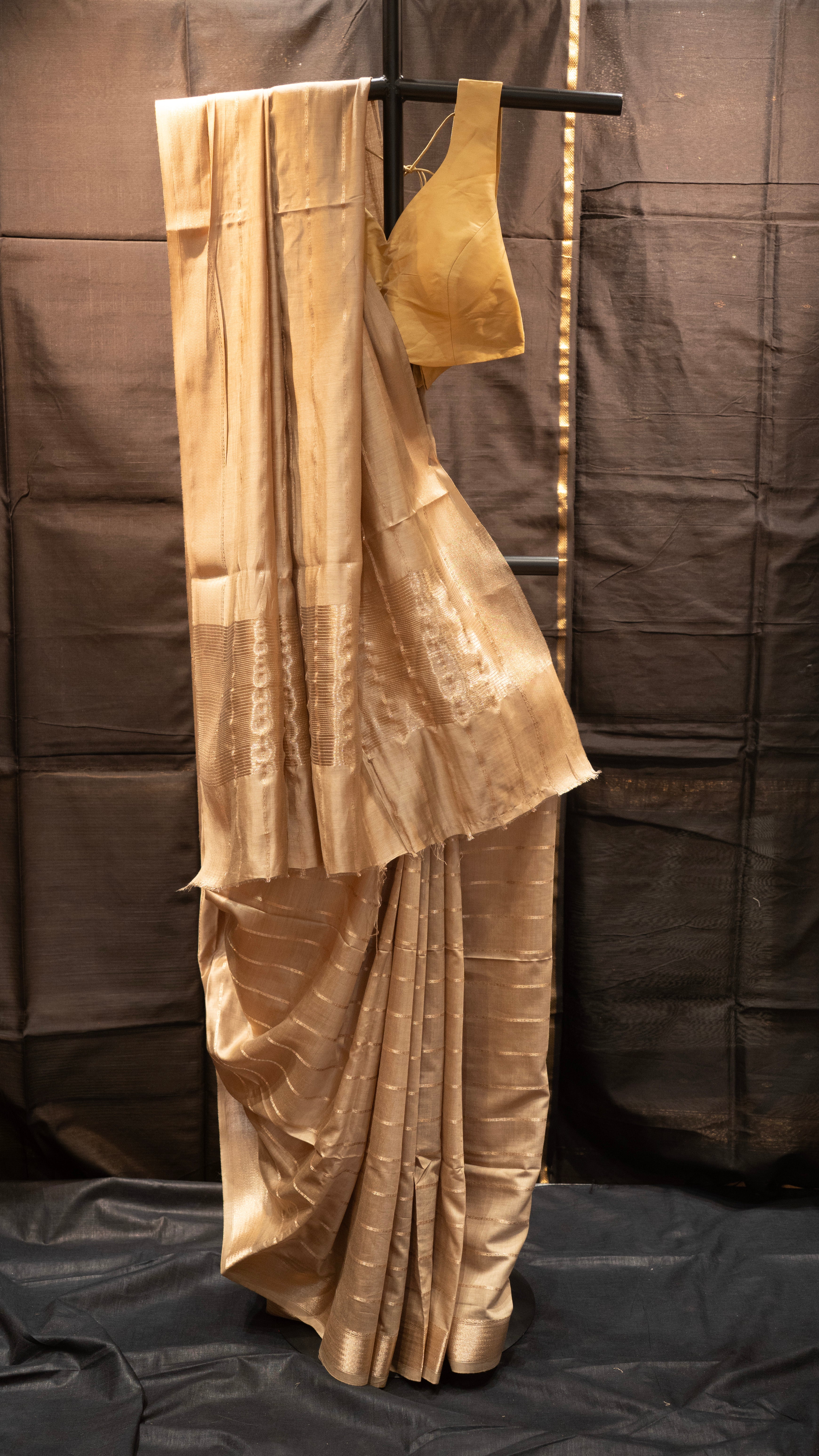 Gold saree with blouse on a black stand against a brown background