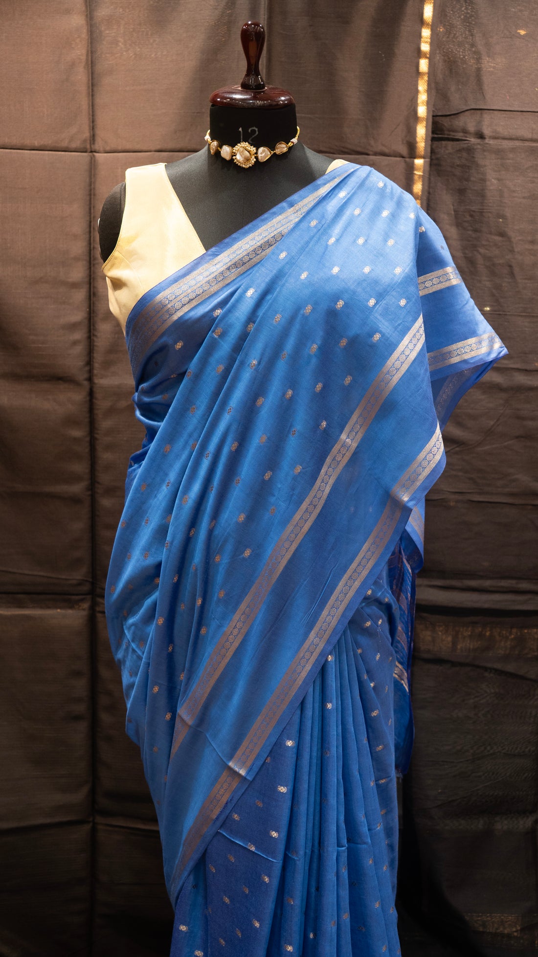 Blue saree with silver border on a mannequin against a brown background