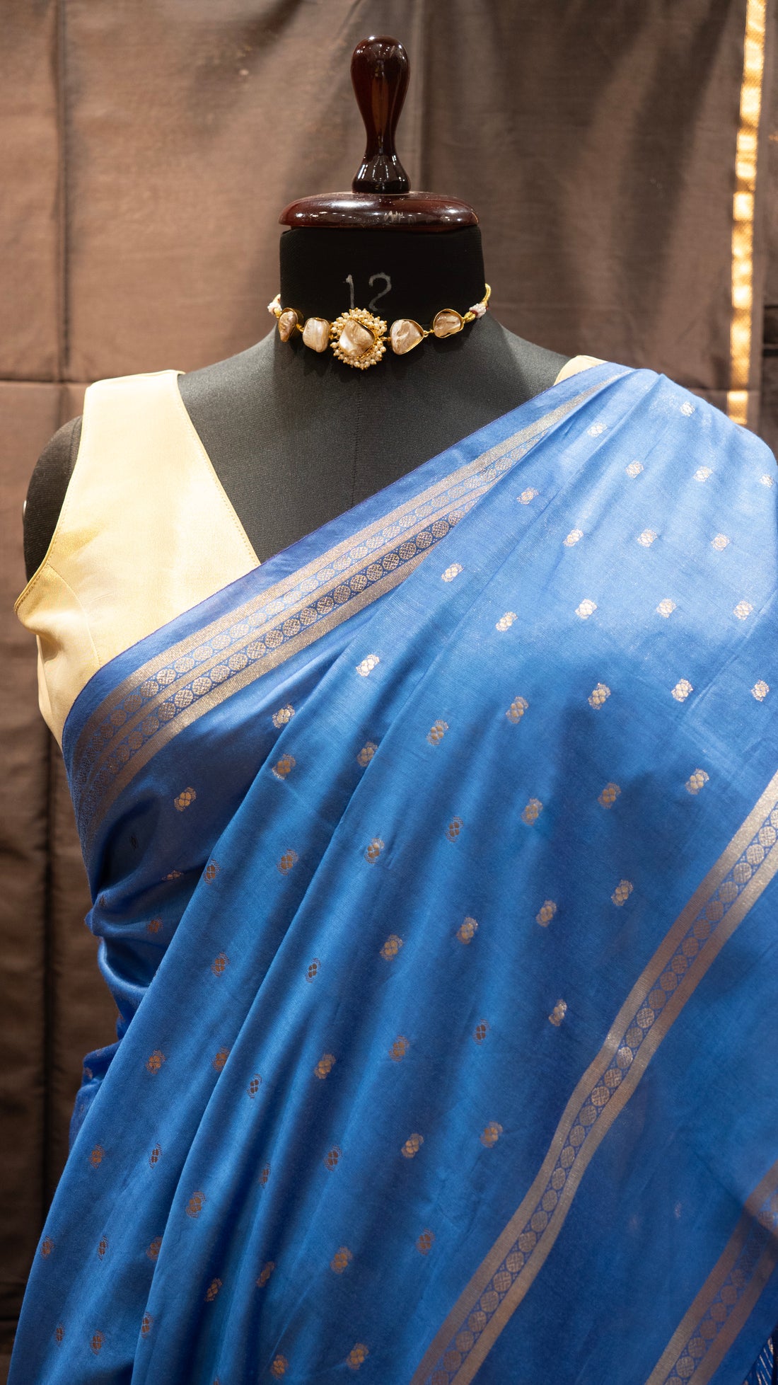 Blue saree with silver border on a mannequin against a brown background