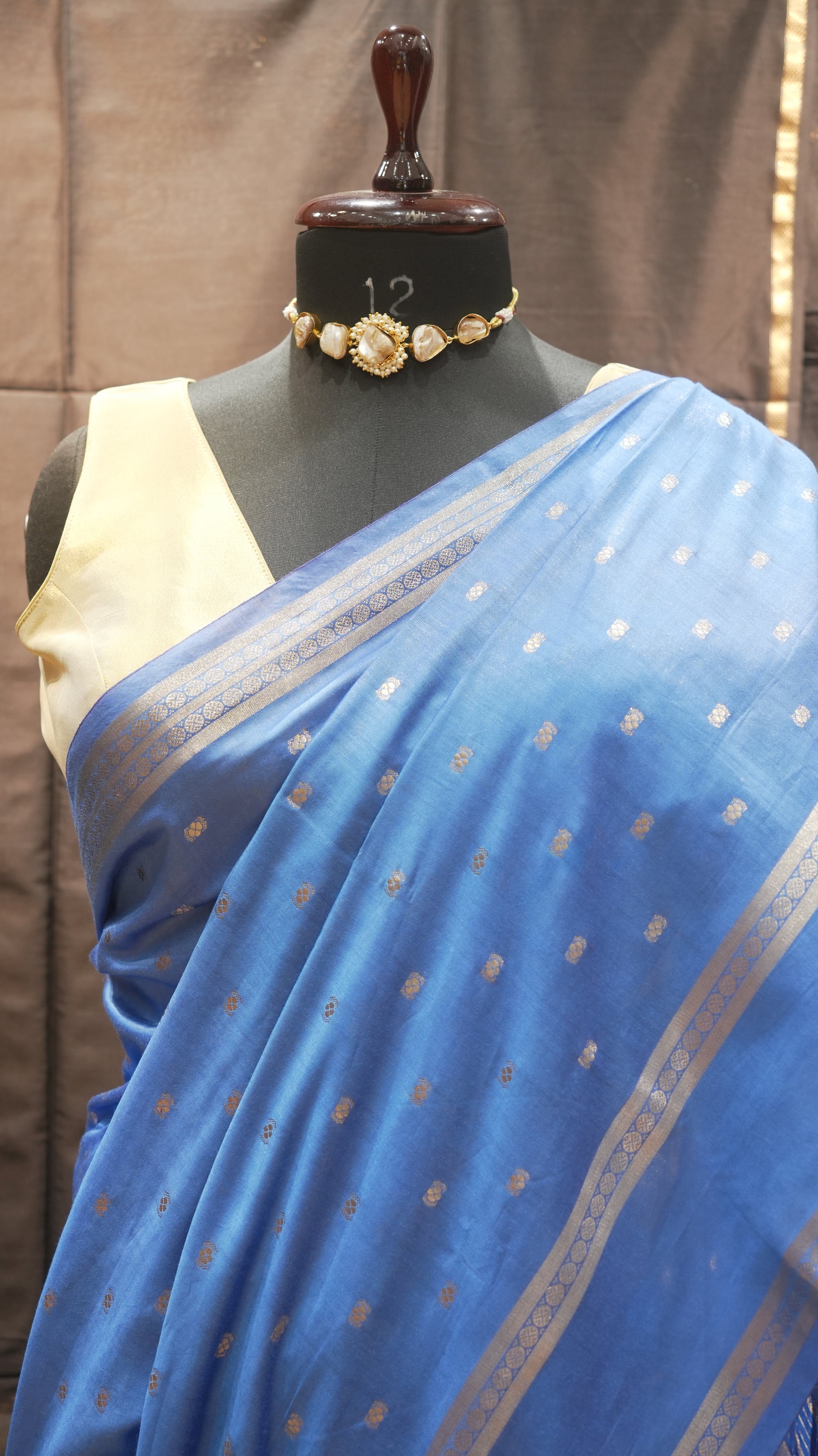Blue saree with gold patterns draped over a mannequin on a neutral background