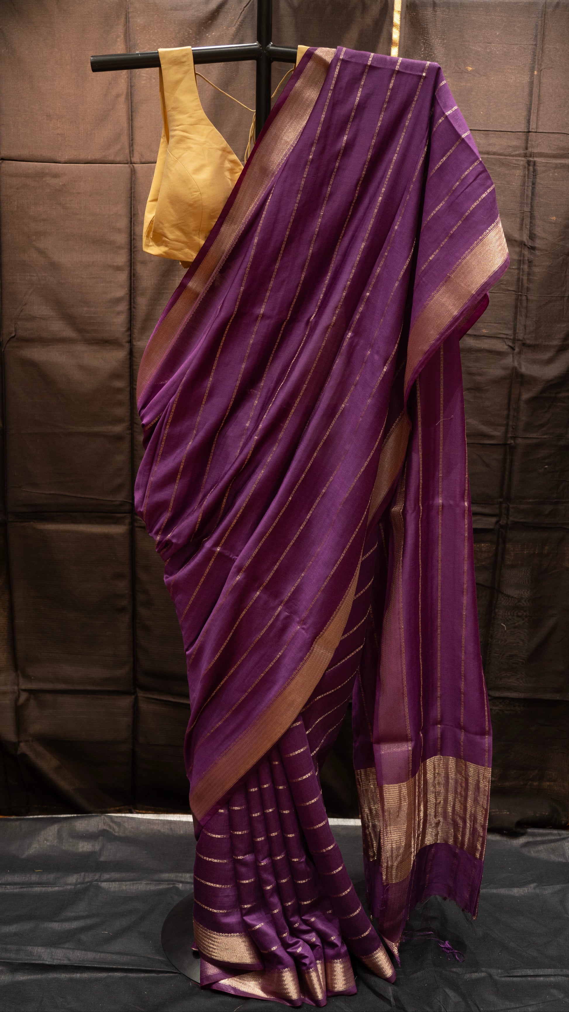 Purple saree with gold border draped over a stand against a brown backdrop