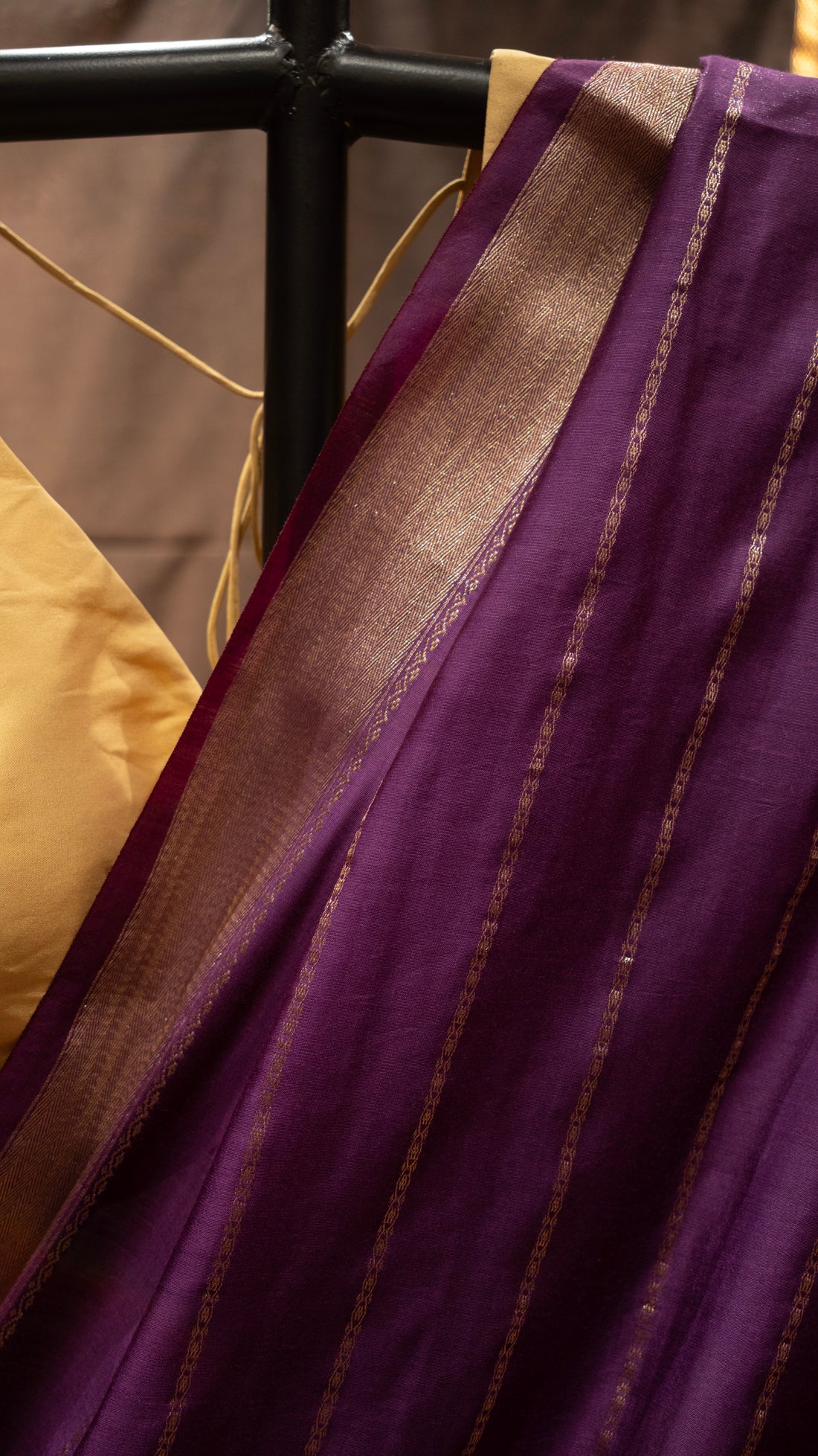 Purple saree with gold border draped over a stand against a brown backdrop