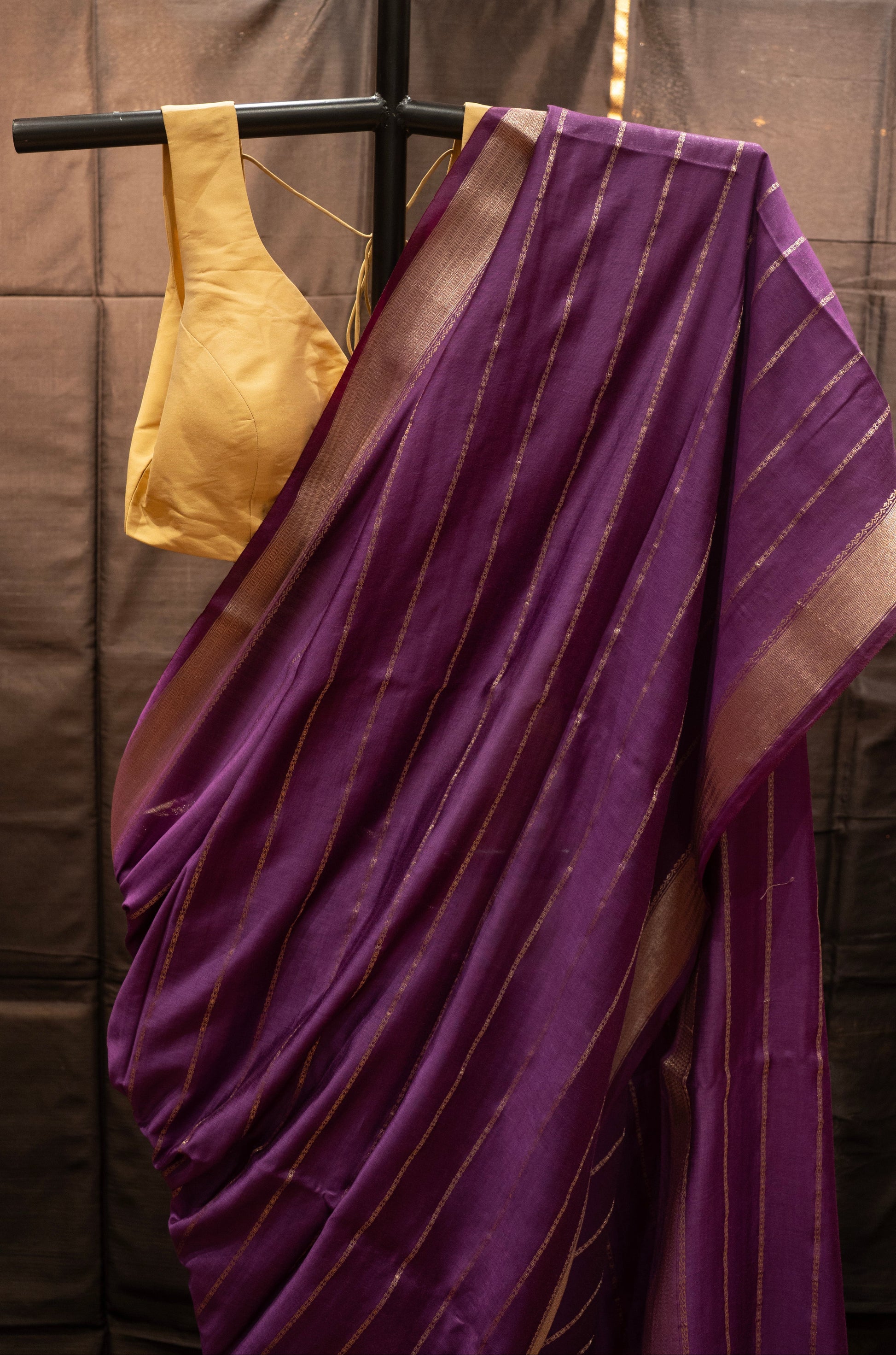 Purple saree with gold border draped over a black rod against a neutral background