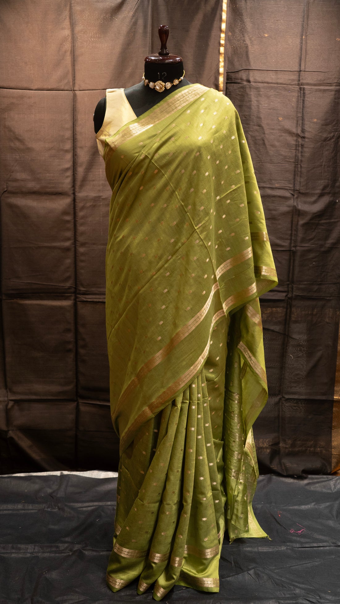 Green saree with gold border on a mannequin against a brown background