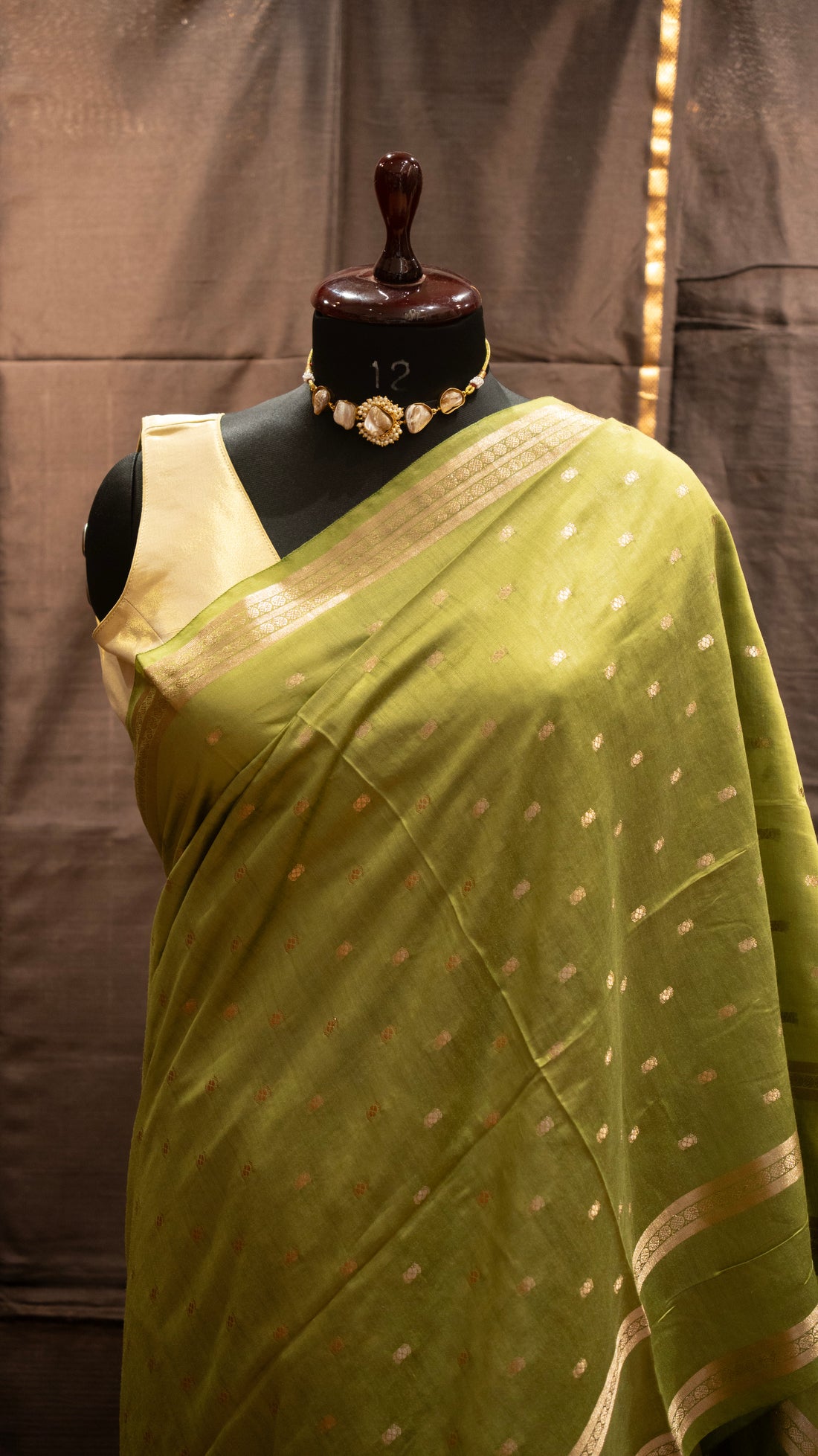Green saree with gold border on a mannequin against a brown background
