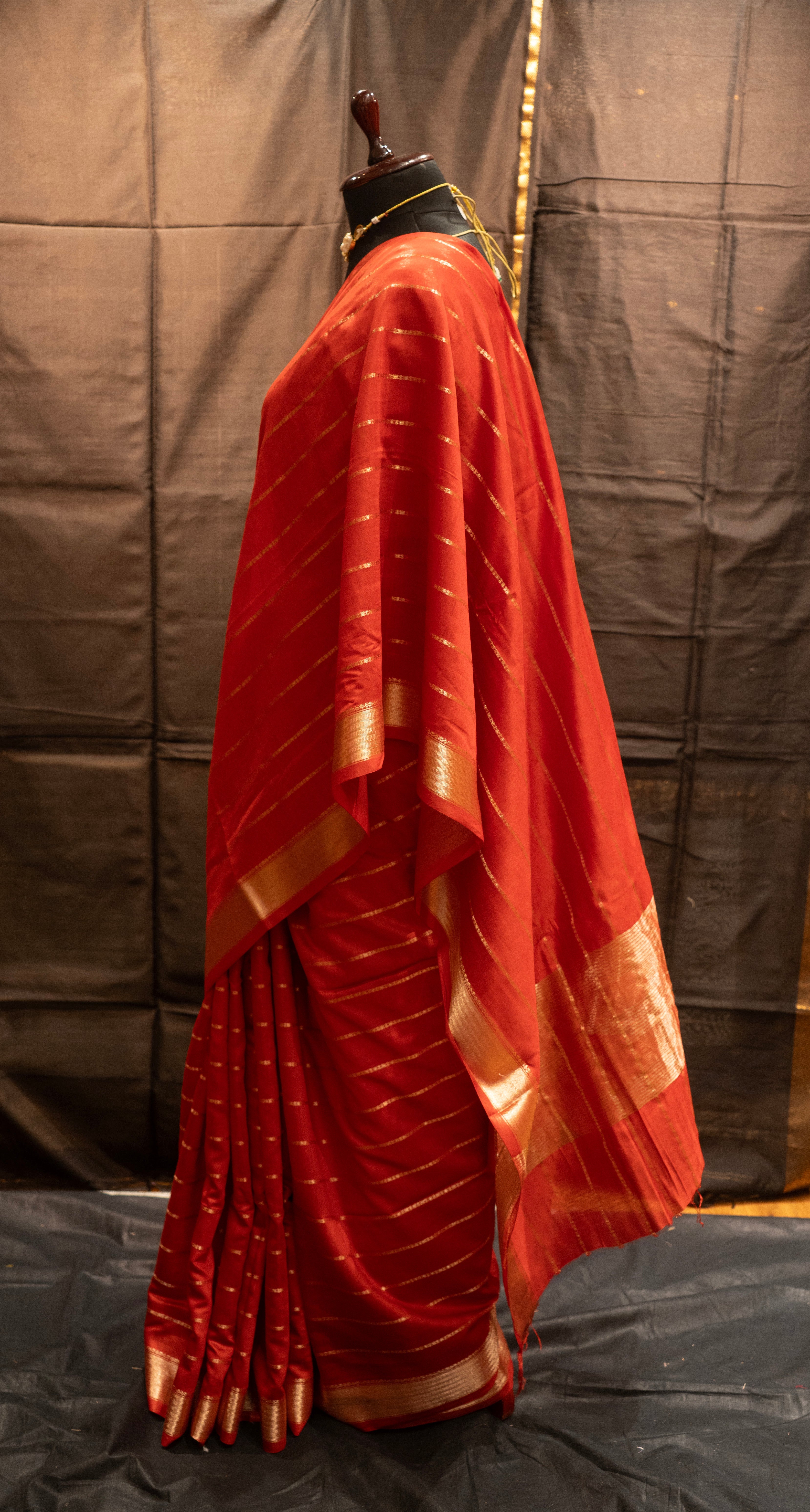 Red saree with gold border on a mannequin against a plain background