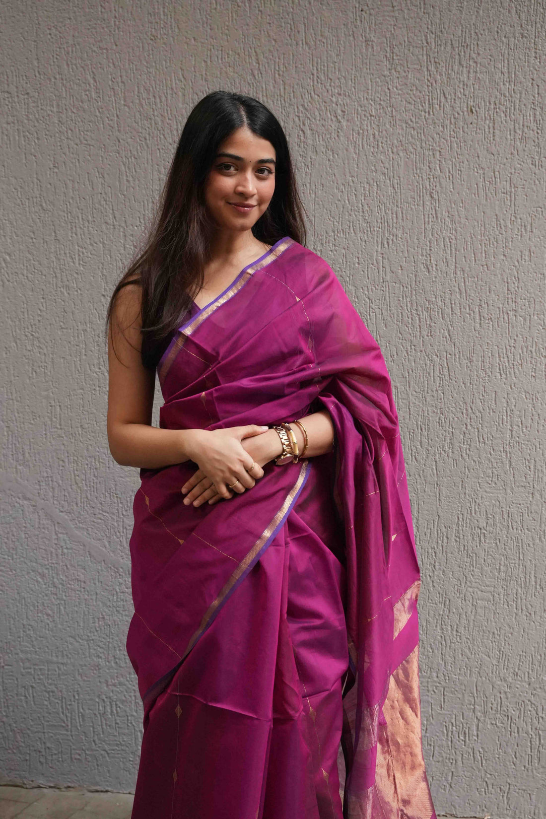 Woman wearing a vibrant pink saree with a subtle pattern against a plain background