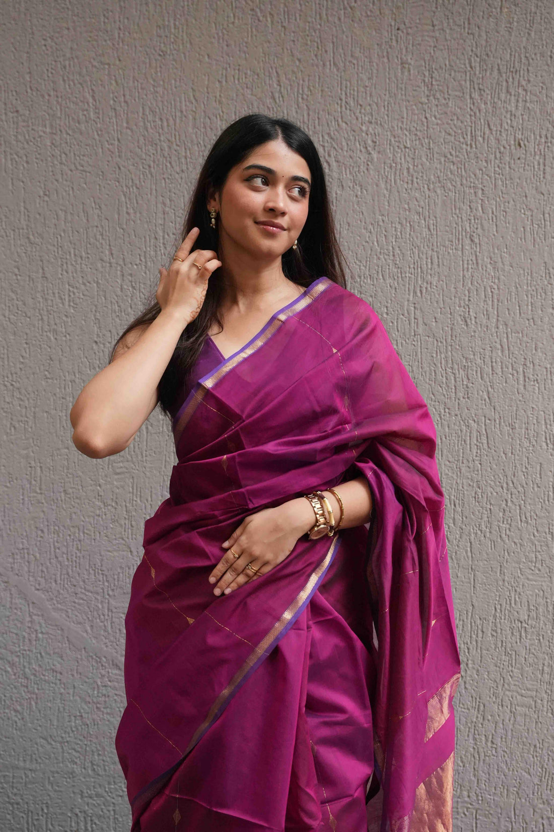 Woman wearing a vibrant pink saree with a subtle pattern against a plain background
