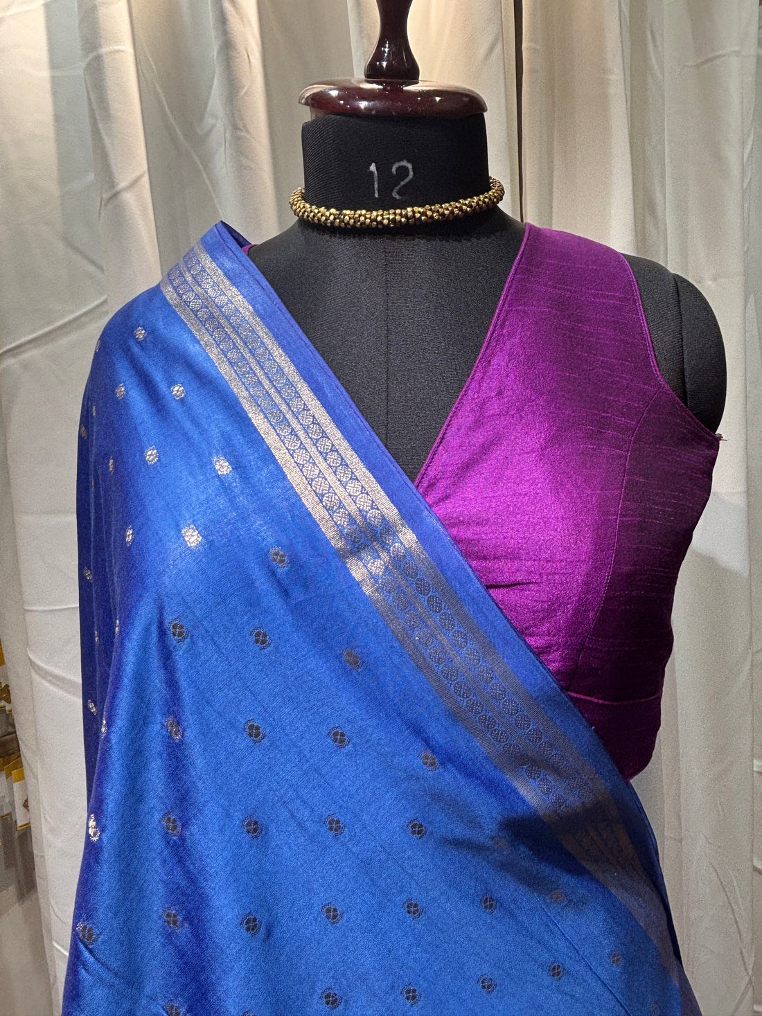 Blue saree with silver border on a mannequin against a wooden floor background