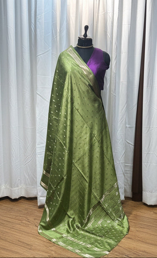 Green fabric on a wooden floor with colorful fabric in the background