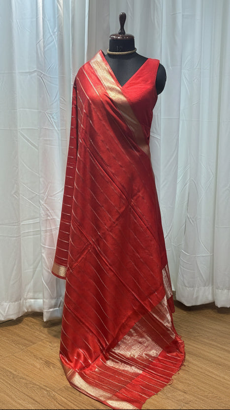 Red saree on a mannequin with a wooden floor and colorful fabrics in the background