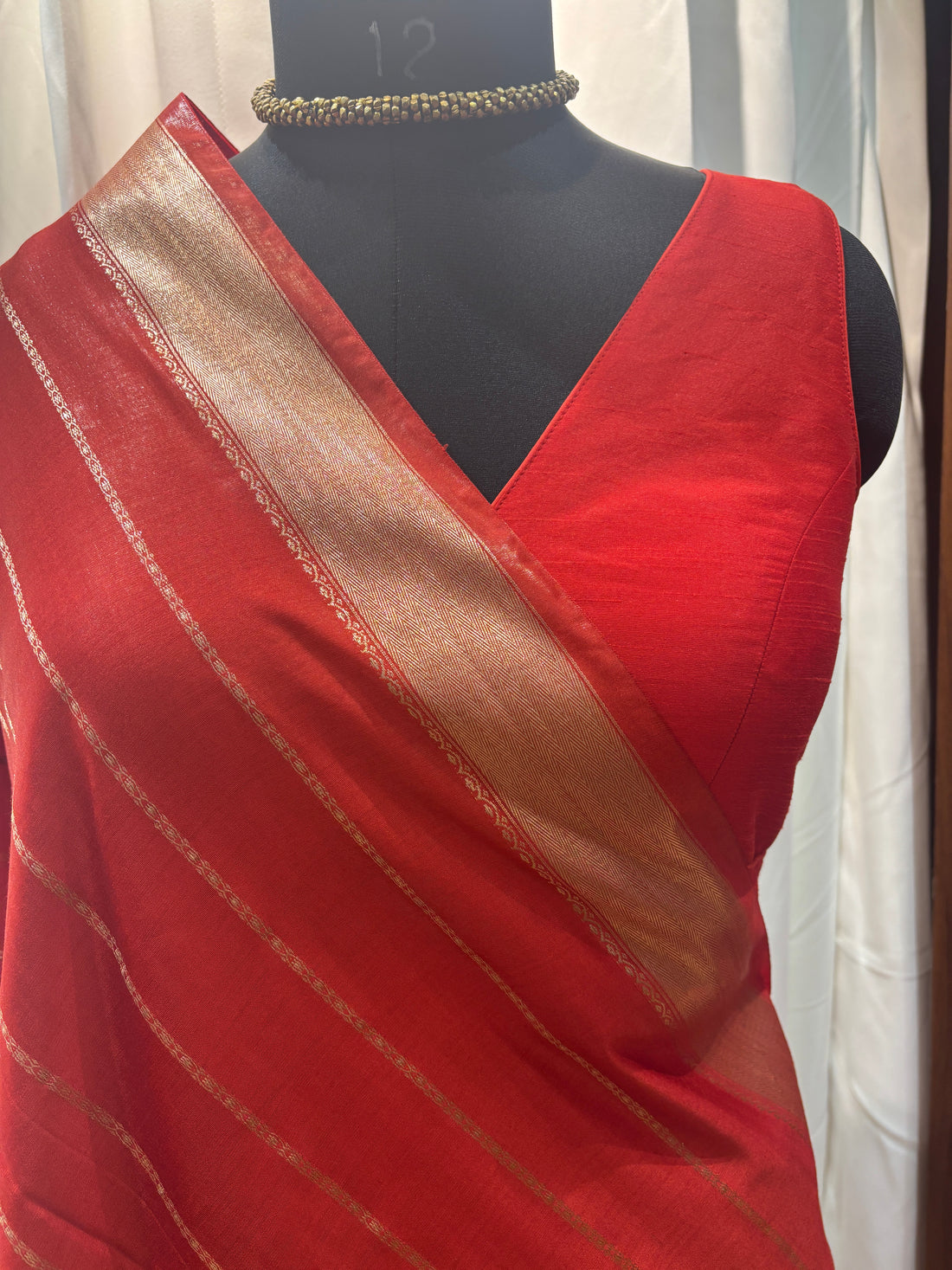 Red saree on a mannequin with a wooden floor and colorful fabrics in the background