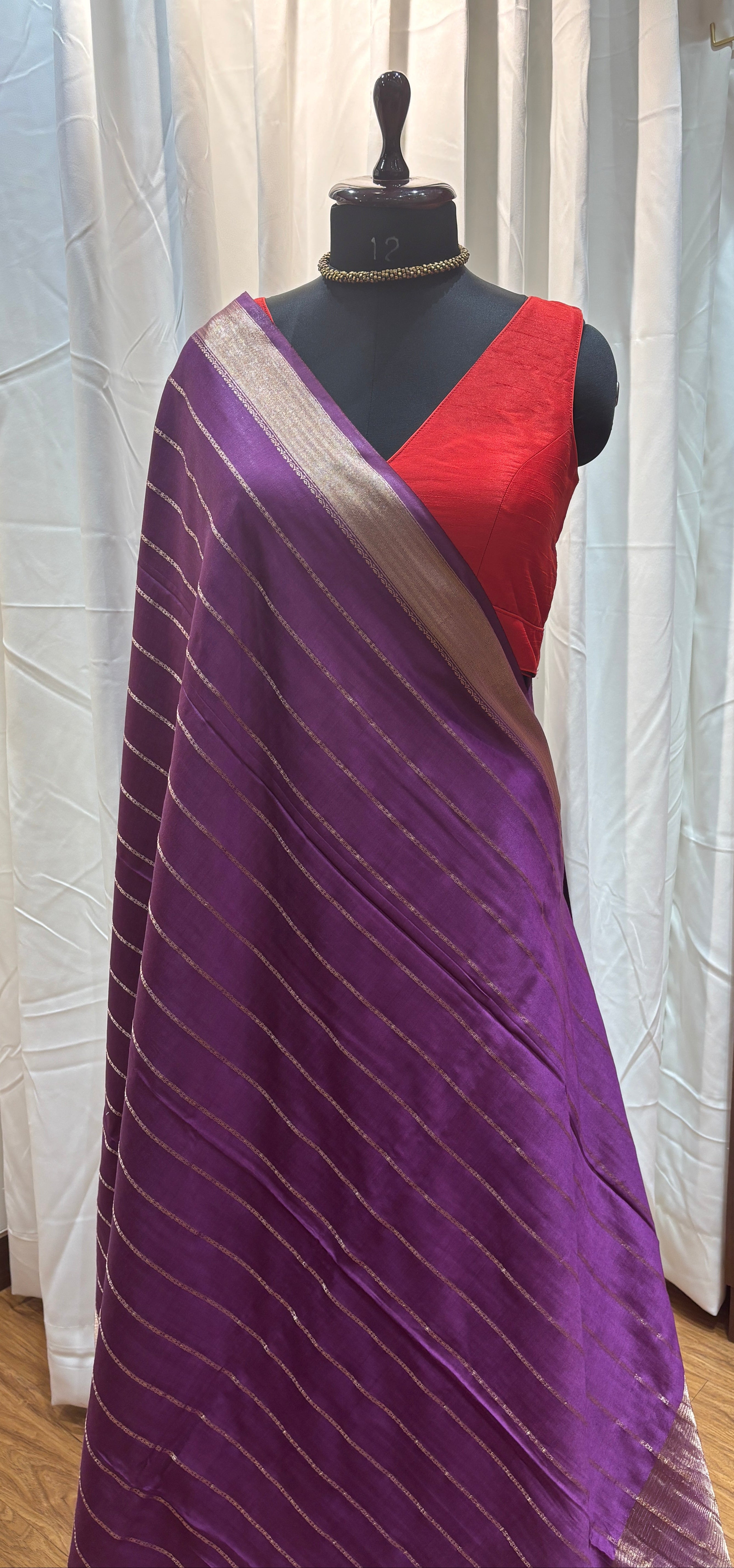 Purple saree draped over a mannequin with a striped fabric background