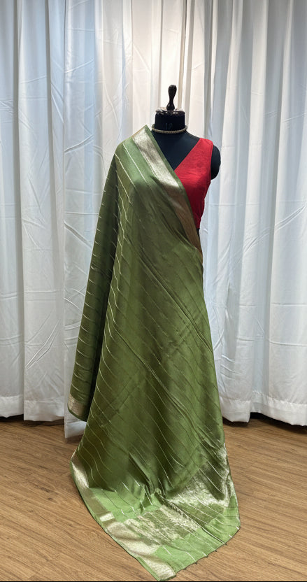 Green fabric on a wooden surface with colorful fabrics in the background